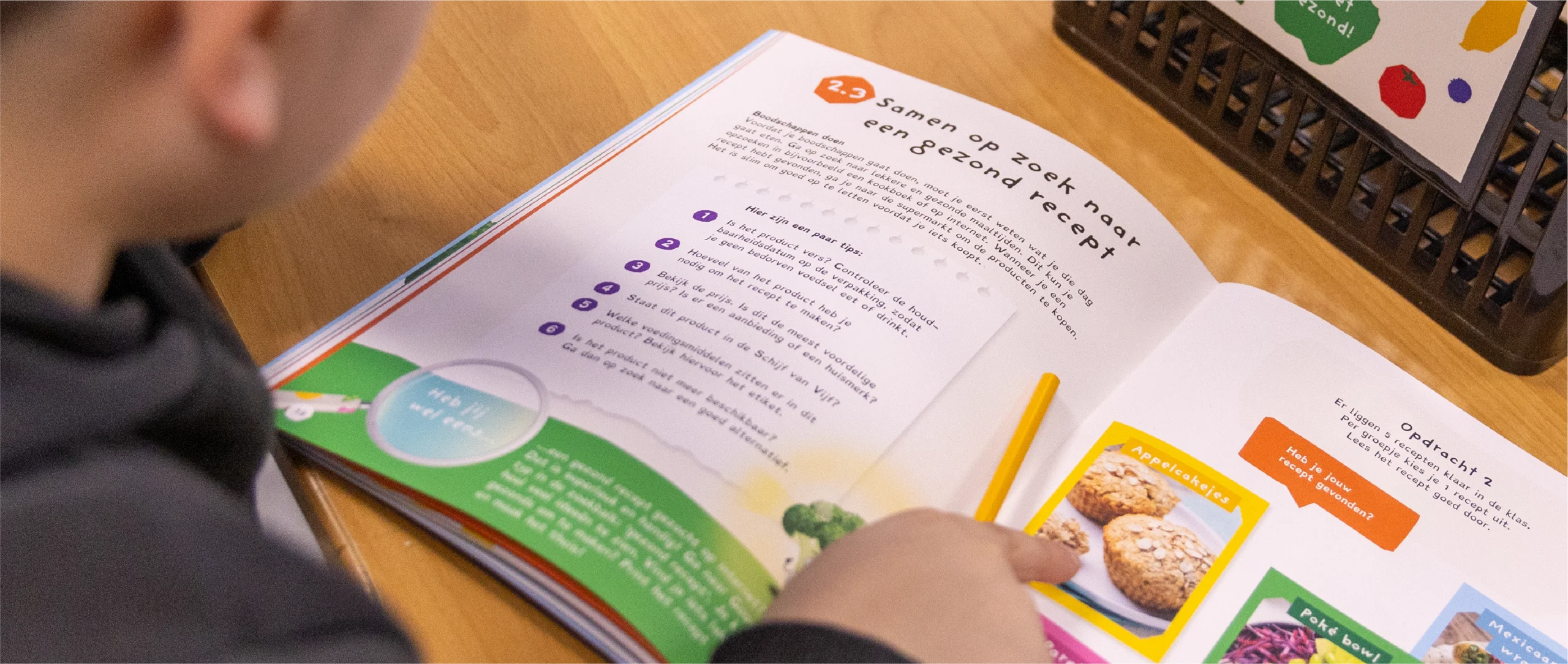 Een kind wijst naar een pagina in de werkboek van "Ik weet gezond"